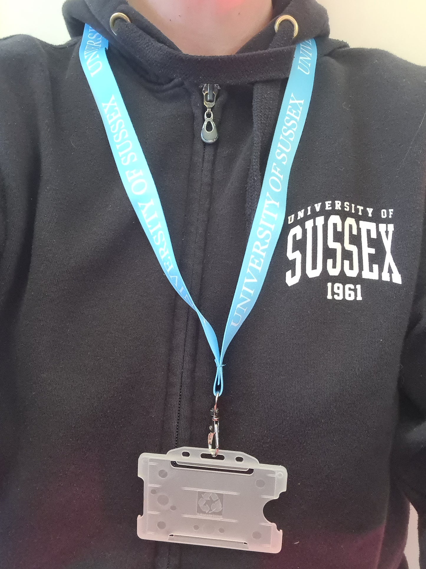 Person wearing a black hoodie with 'University of Sussex 1961' text, wearing a light blue lanyard with a badge holder that says University of Sussex around it.