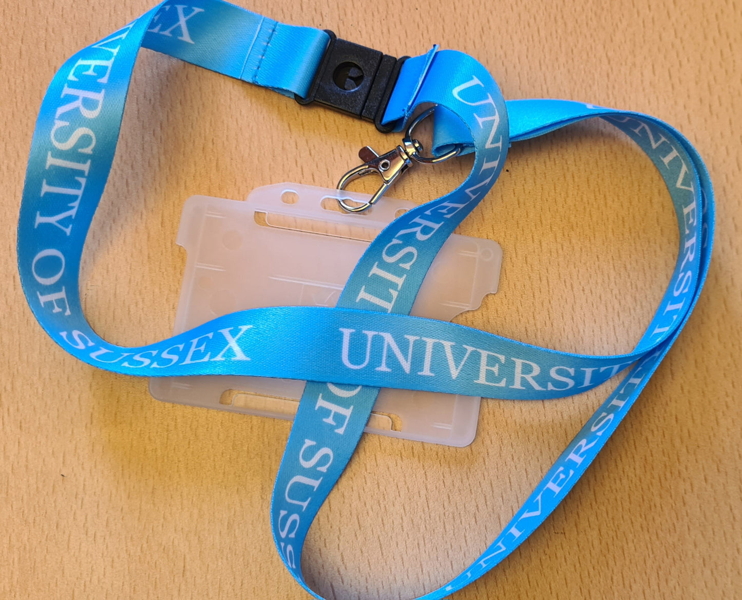 Light blue lanyard with 'University of Sussex' text and a card holder on a wooden surface