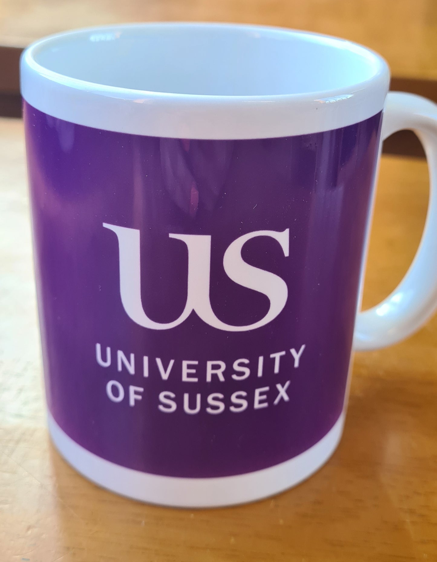 Grape mug with the 'US University of Sussex' logo on a wooden surface