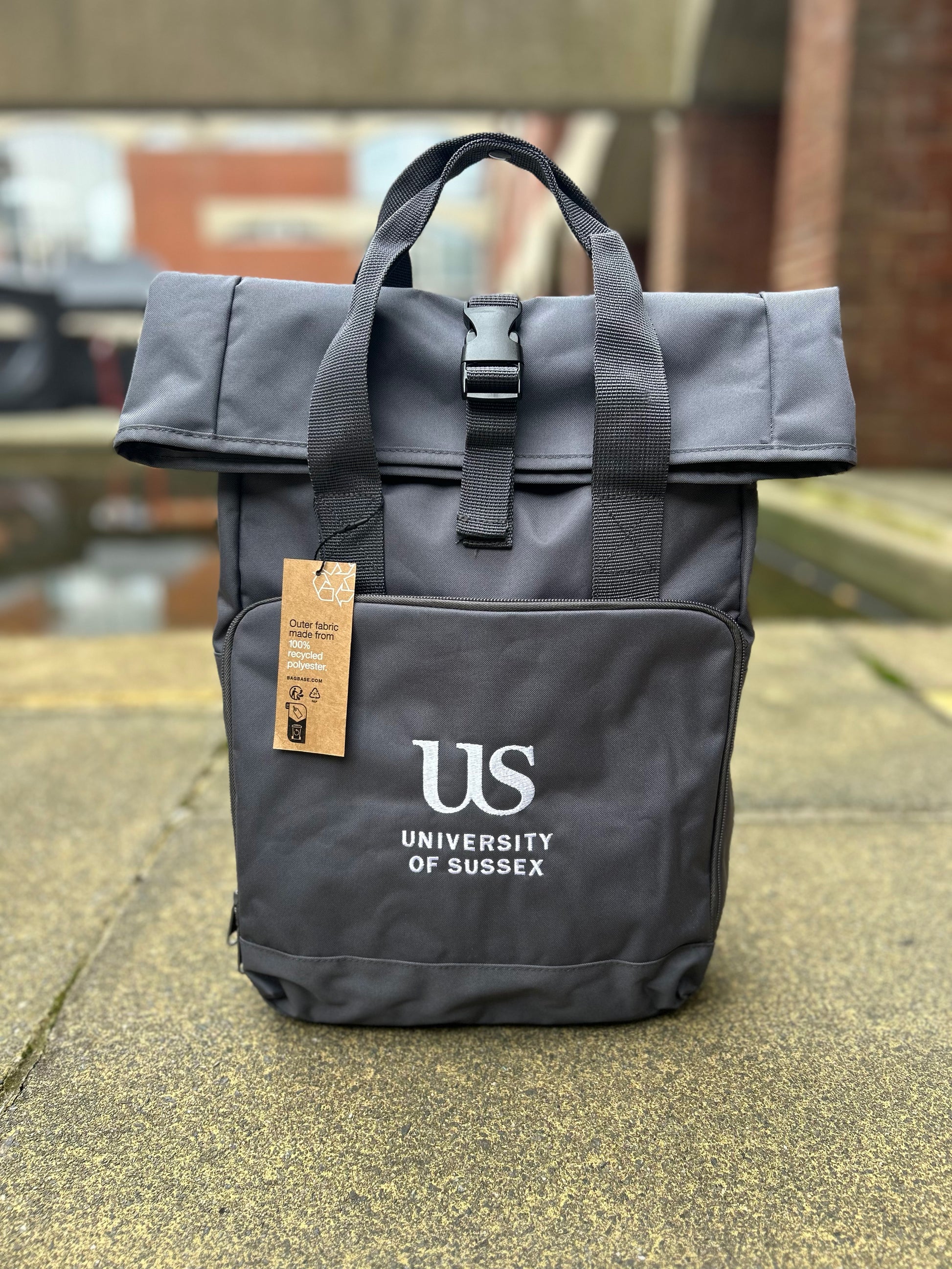 Charcoal backpack with 'US University of Sussex' logo on a pavement